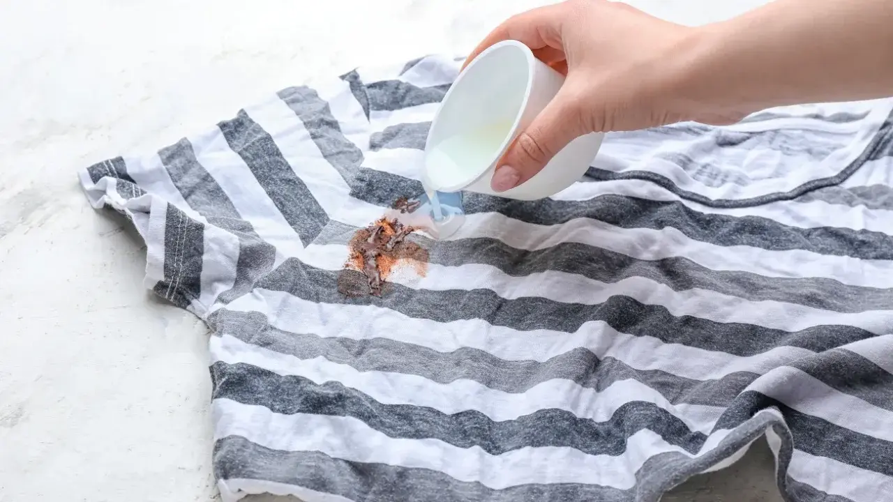 Plama z czekolady na pasiastym t-shircie, na którą wylewany jest płyn.