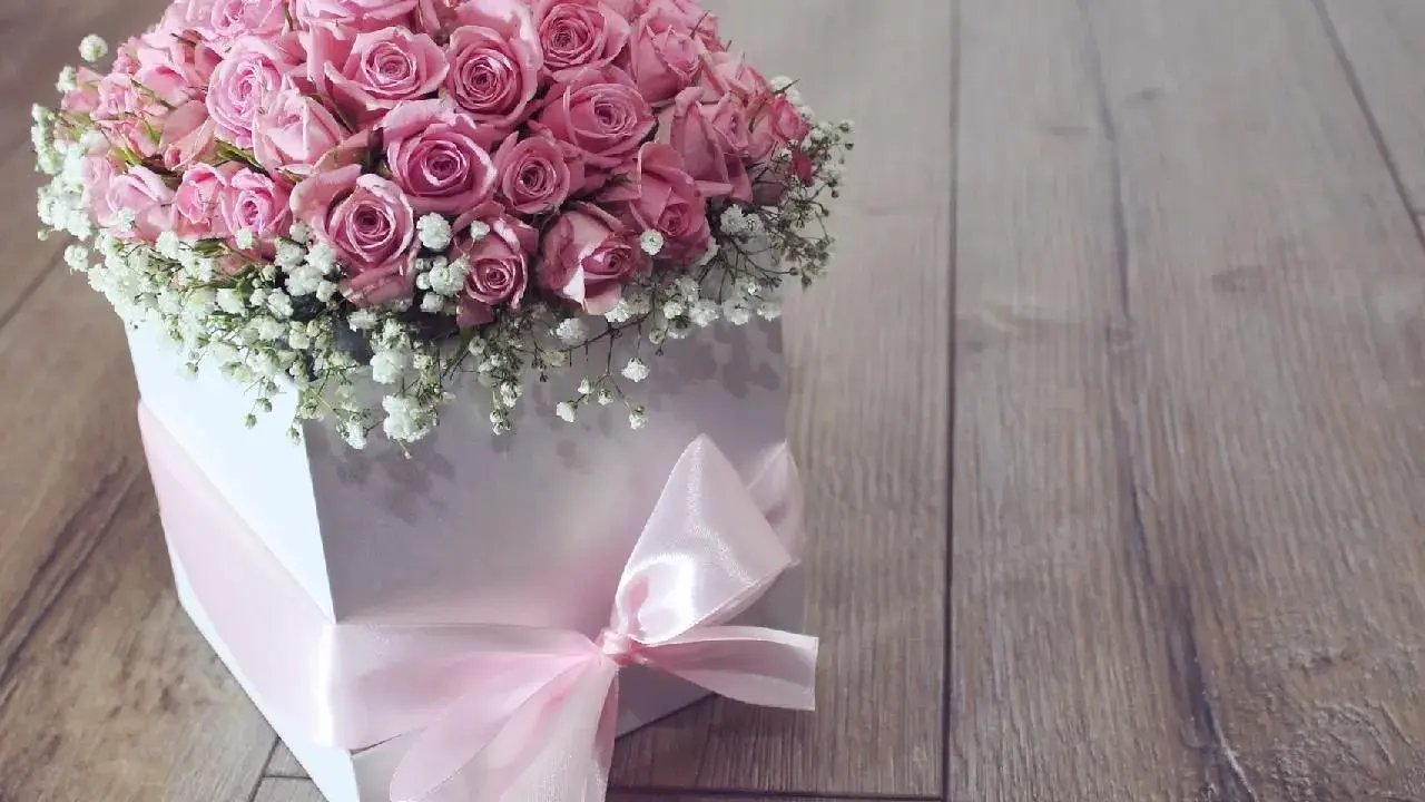 Piękny flower box jak zrobić? Bukiet róż w białym pudełku, ozdobiony różową wstążką, na drewnianym tle.