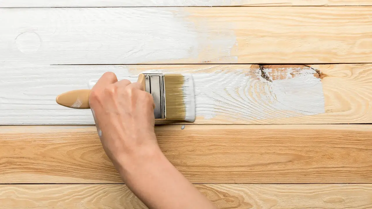 Ręka maluje pędzlem drewnianą boazerię na biało. Dowiedz się, jak odnowić boazerię.