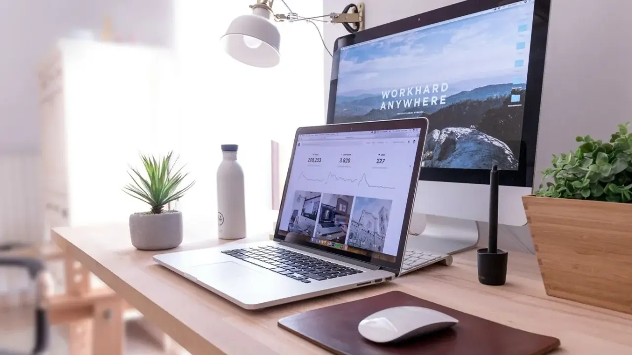 Idealna organizacja biurka w pracy: laptop, monitor, lampka, roślina i butelka wody.