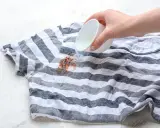 Plama z czekolady na pasiastym t-shircie, na którą wylewany jest płyn.