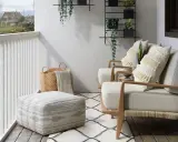 Wąski balkon w bloku inspiracje: przytulne fotele, pufy, kosze i rośliny tworzą oazę spokoju.