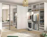 Zorganizowana garderoba w stylu Marie Kondo: białe fronty, lustrzane drzwi, półki z pudełkami i wieszaki z ubraniami.