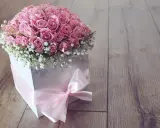 Piękny flower box jak zrobić? Bukiet róż w białym pudełku, ozdobiony różową wstążką, na drewnianym tle.