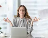 Kobieta w biurze medytuje, ignorując chaos wokół. Pokazuje, jak zadbać o siebie psychologia w stresujących sytuacjach.
