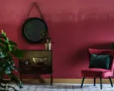Eleganckie wnętrze w odcieniu **kolor marsala**. Aksamitny fotel, lustro i stylowa komoda tworzą przytulną atmosferę.