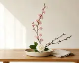 Delikatna ikebana: gałązka kwitnącej wiśni, biała kamelia i bazie w ceramicznej misie. Sztuka układania kwiatów, która uspokaja.