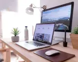 Idealna organizacja biurka w pracy: laptop, monitor, lampka, roślina i butelka wody.