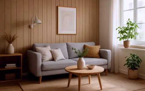 Przytulny salon z szarą kanapą, drewnianymi panelami ściennymi i roślinami. Inspiracje malowanie paneli ściennych w naturalnych barwach.
