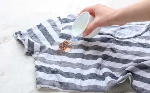 Plama z czekolady na pasiastym t-shircie, na którą wylewany jest płyn.