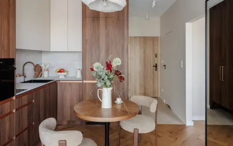Przytulna jadalnia w stylu mid century z okrągłym stołem, dwoma fotelami i bukietem kwiatów.