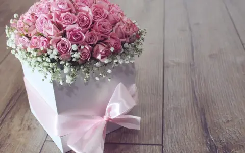 Piękny flower box jak zrobić? Bukiet róż w białym pudełku, ozdobiony różową wstążką, na drewnianym tle.