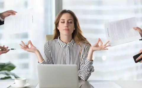 Kobieta w biurze medytuje, ignorując chaos wokół. Pokazuje, jak zadbać o siebie psychologia w stresujących sytuacjach.