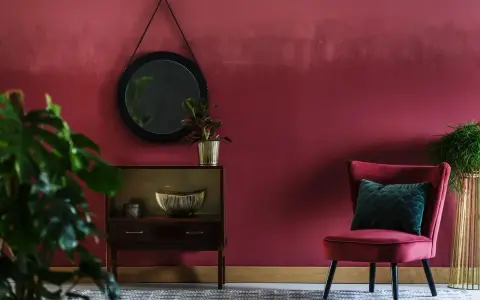 Eleganckie wnętrze w odcieniu **kolor marsala**. Aksamitny fotel, lustro i stylowa komoda tworzą przytulną atmosferę.