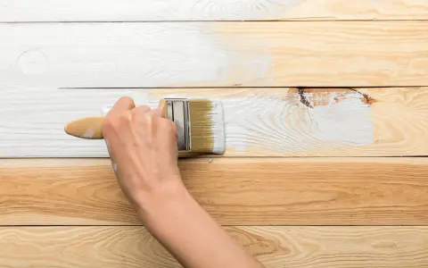 Ręka maluje pędzlem drewnianą boazerię na biało. Dowiedz się, jak odnowić boazerię.
