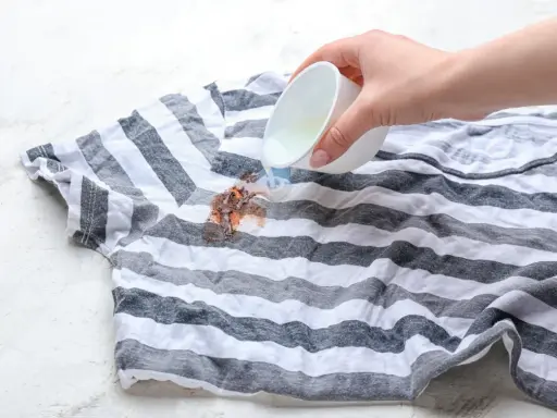 Plama z czekolady na pasiastym t-shircie, na którą wylewany jest płyn.