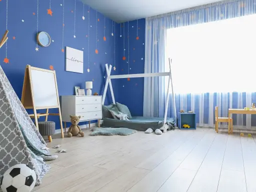 Pokój dziecka z niebieskimi, malowanymi ścianami ozdobionymi gwiazdkami. W rogu stoi namiot tipi, obok łóżko i komoda.