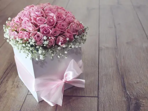 Piękny flower box jak zrobić? Bukiet róż w białym pudełku, ozdobiony różową wstążką, na drewnianym tle.