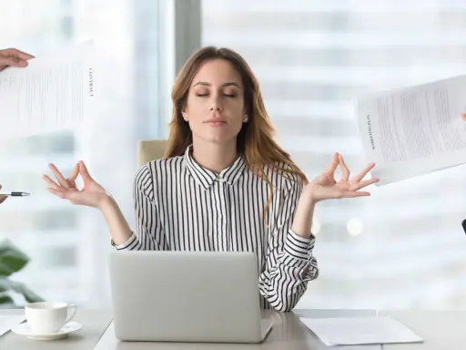 Kobieta w biurze medytuje, ignorując chaos wokół. Pokazuje, jak zadbać o siebie psychologia w stresujących sytuacjach.
