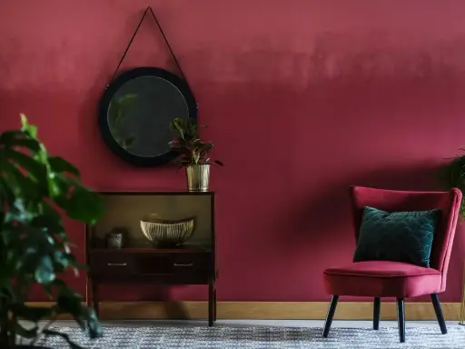 Eleganckie wnętrze w odcieniu **kolor marsala**. Aksamitny fotel, lustro i stylowa komoda tworzą przytulną atmosferę.