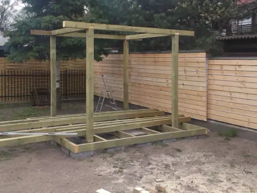 Budowa altanki z palet w ogrodzie. Drewniana konstrukcja z fundamentem z bloczków betonowych, gotowa na dalsze prace.