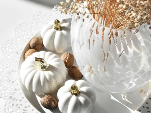 Białe dynie z złotymi łodyżkami i orzechy włoskie tworzą eleganckie jesienne dekoracje DIY. W tle wazon z suszonymi kwiatami.