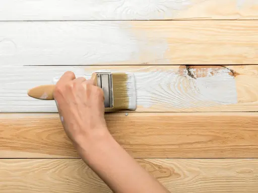 Ręka maluje pędzlem drewnianą boazerię na biało. Dowiedz się, jak odnowić boazerię.