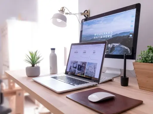 Idealna organizacja biurka w pracy: laptop, monitor, lampka, roślina i butelka wody.