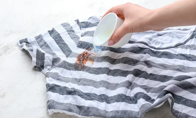 Plama z czekolady na pasiastym t-shircie, na którą wylewany jest płyn.