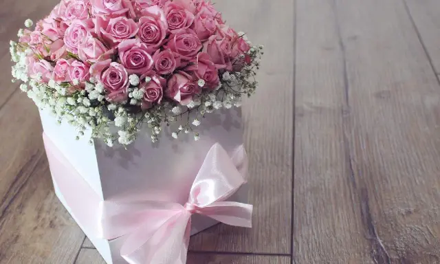 Piękny flower box jak zrobić? Bukiet róż w białym pudełku, ozdobiony różową wstążką, na drewnianym tle.
