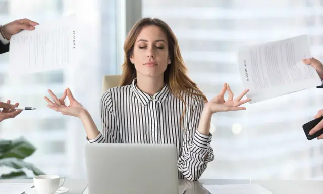 Kobieta w biurze medytuje, ignorując chaos wokół. Pokazuje, jak zadbać o siebie psychologia w stresujących sytuacjach.