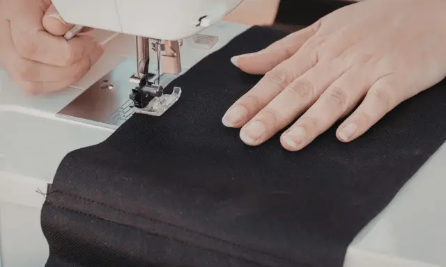 Ręce szyją czarną tkaninę na maszynie. Powstaje torba DIY.