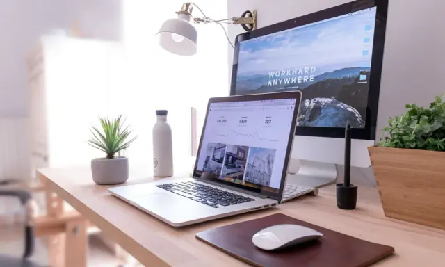 Idealna organizacja biurka w pracy: laptop, monitor, lampka, roślina i butelka wody.