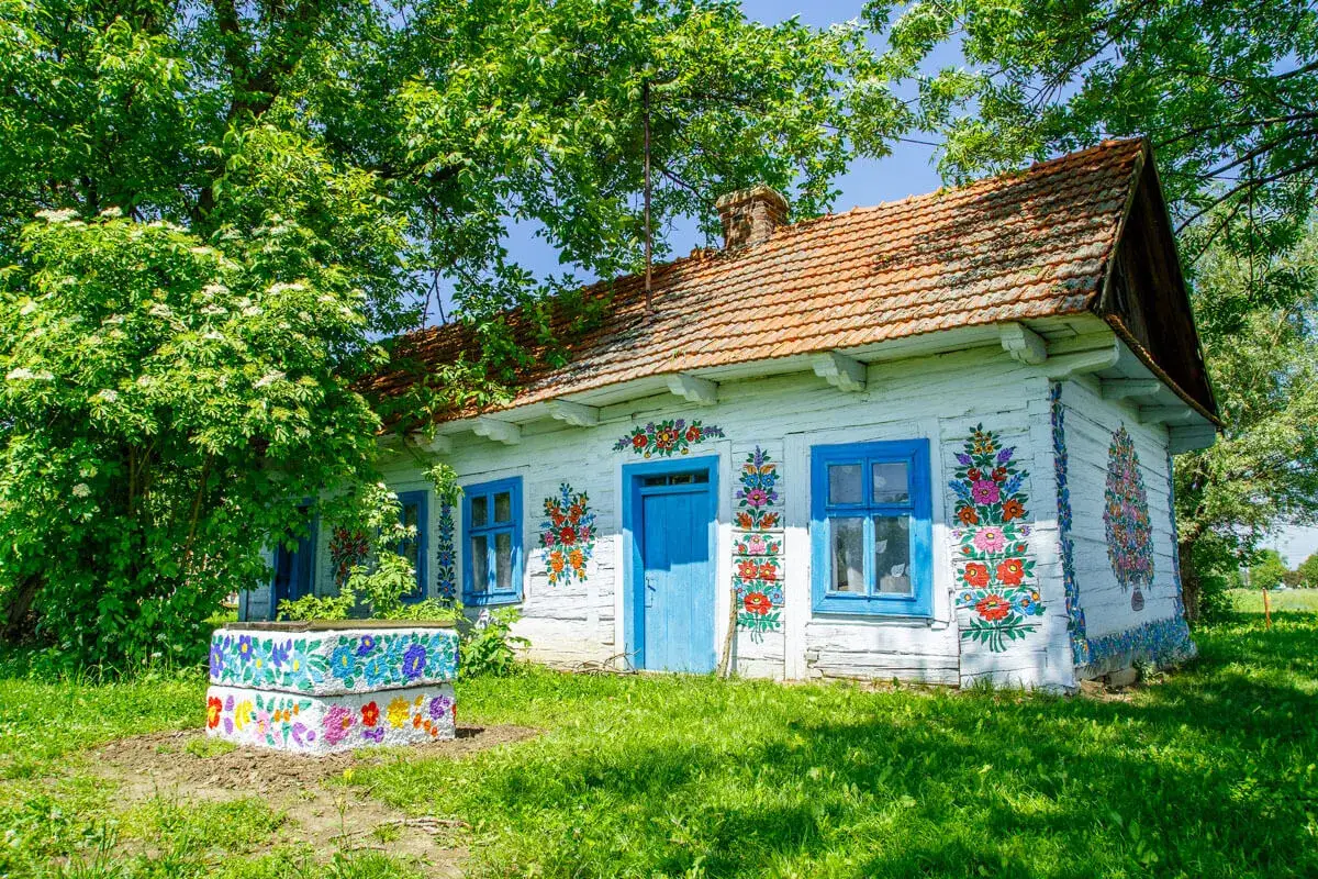 Kolorowy dom z ludowymi wzorami, kwitnące drzewa i zielona trawa. To prawdziwe życie na wsi, pełne barw i spokoju.