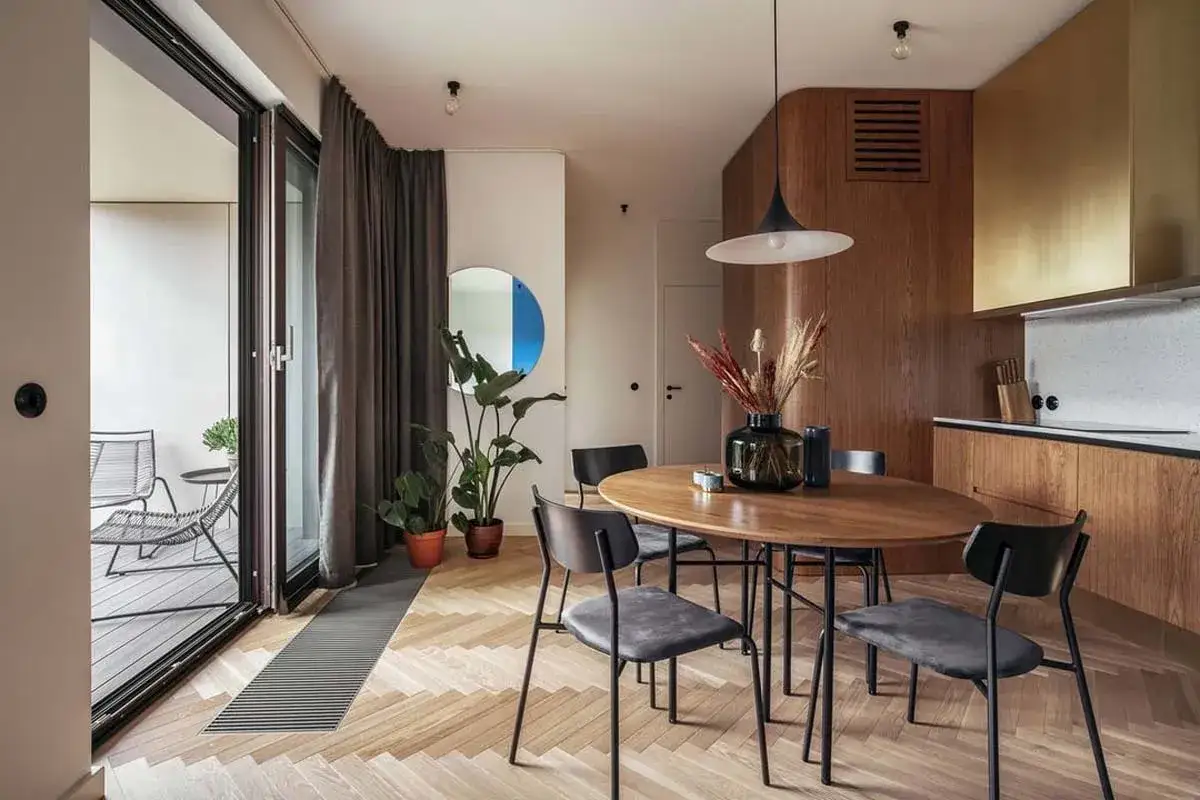 Jadalnia w stylu mid century z okrągłym drewnianym stołem, czarnymi krzesłami i bujną roślinnością.