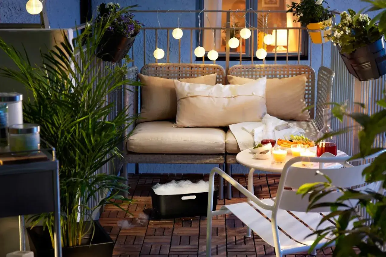 Wąski balkon w bloku inspiracje: przytulna kanapa, stolik z przekąskami i świecami, rośliny i girlanda świetlna tworzą relaksującą atmosferę.
